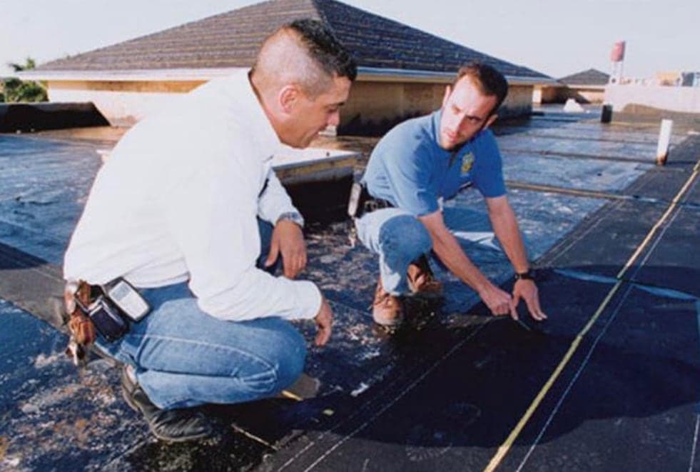 Two men going over a flat roof by hand.