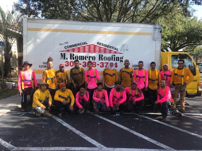 El equipo de M. Romero's Roofing con las camisas rosadas y de alta visibilidad que usan cada octubre por la concientización sobre el cáncer de mama, frente al camión de caja.