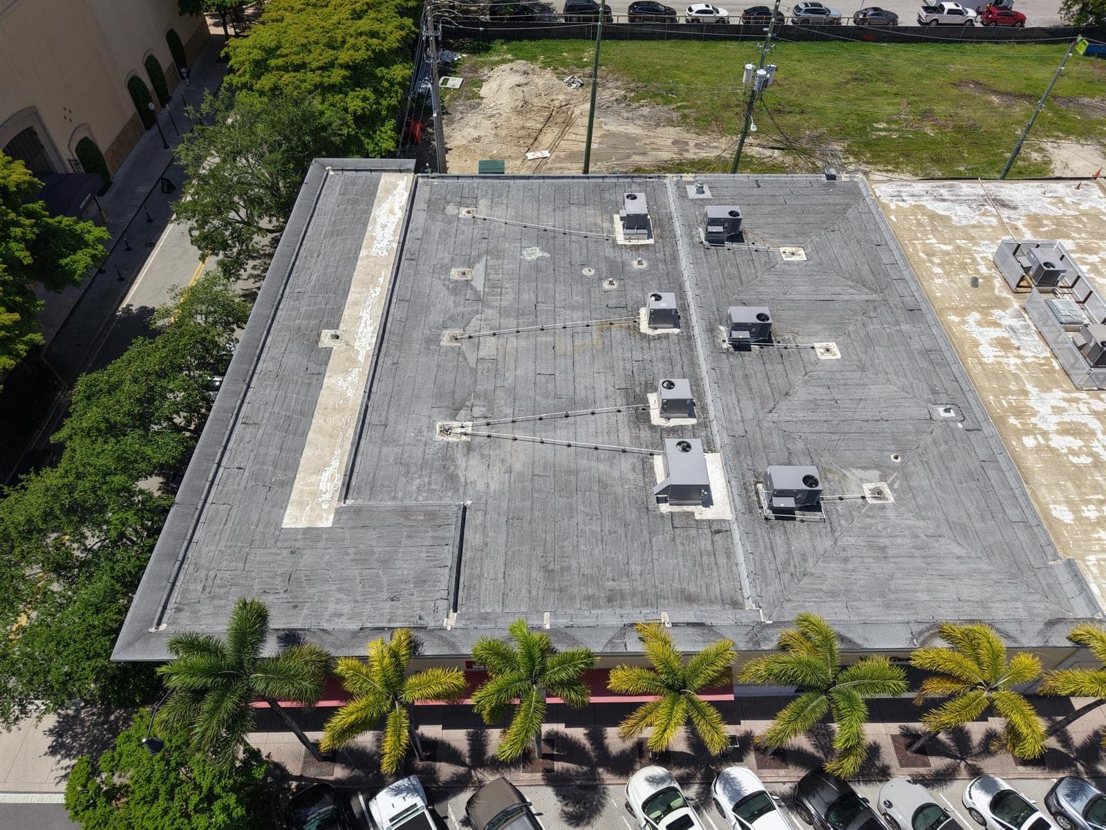 A commercial flat roof from the air, streaked grey modified bitumen before coating.