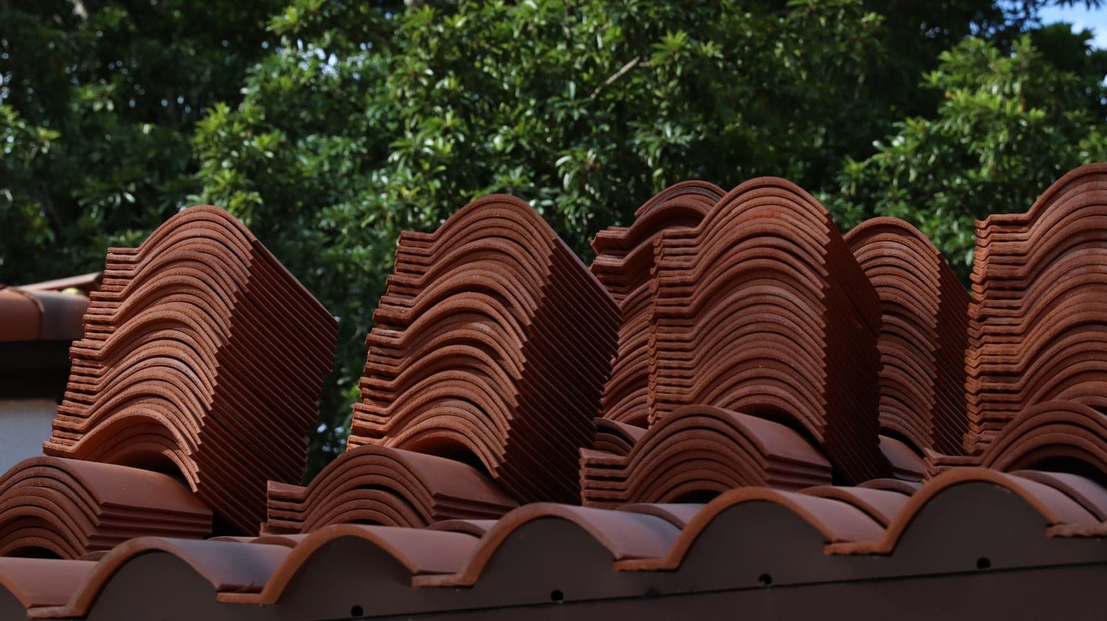 Bundles of new terracotta Spanish S-tile stacked on a roof deck, ready to be laid.